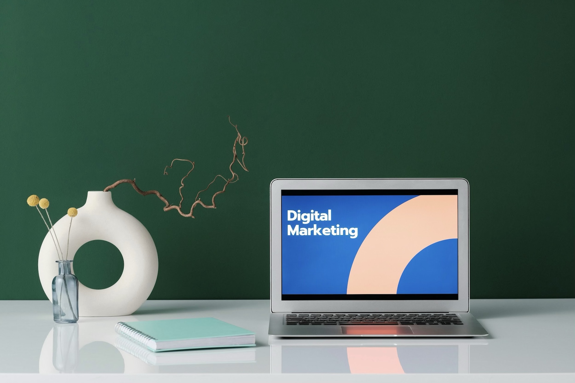 Laptop monitor showing the words digital marketing next to two vases and a blue notebook